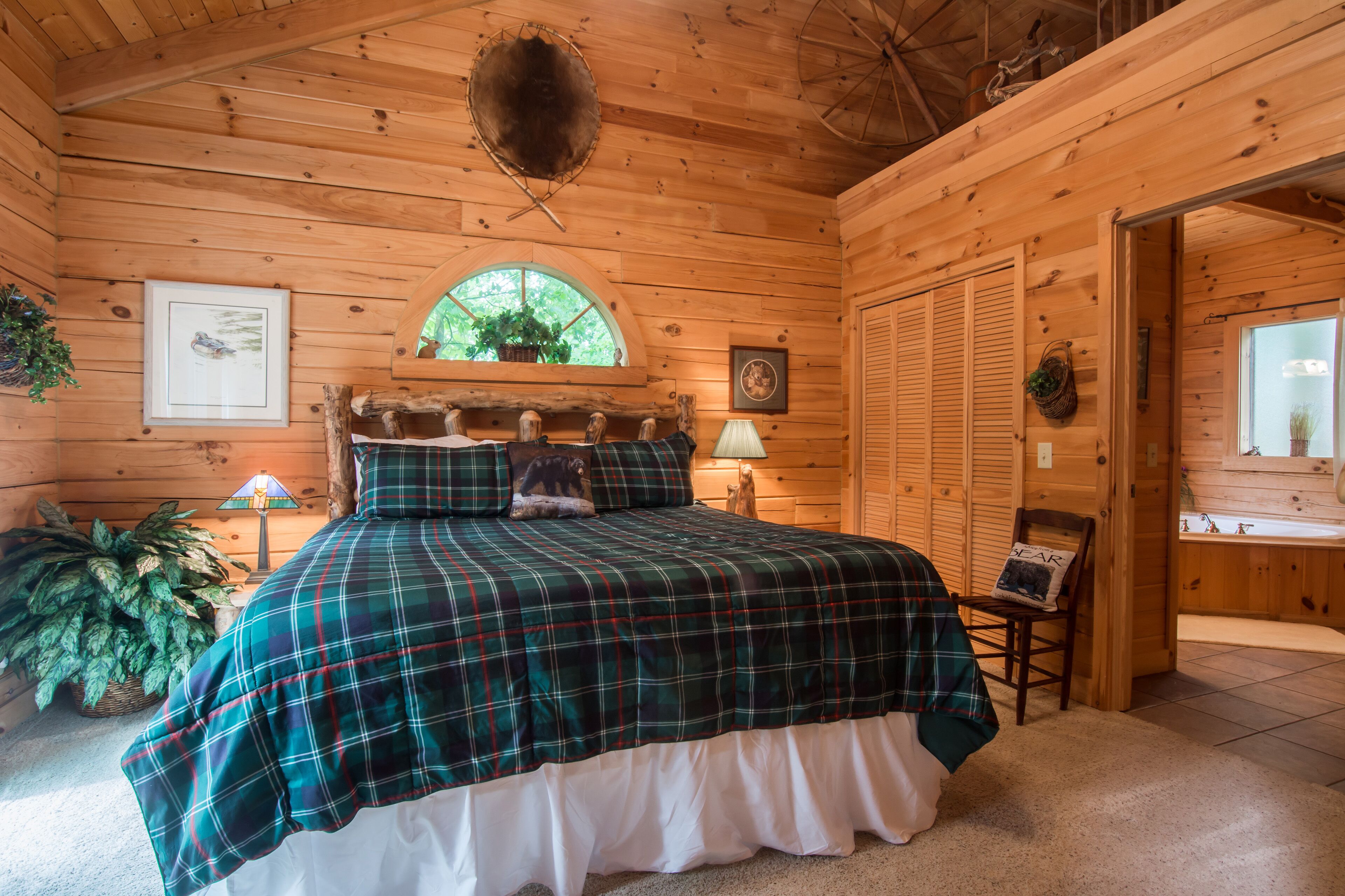Une chambre à coucher dans une cabane en bois, avec une couvre-lit à carreaux, une fenêtre donnant sur un paysage agréable et un plafond en bois.