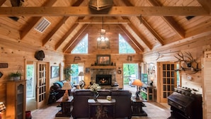 A log cabin interior with a fireplace, wooden beams, and a cozy seating area. - Two Master Suites, Great for 2 couples, Walking distance to Thunder Ridge Arena (Ridgedale)