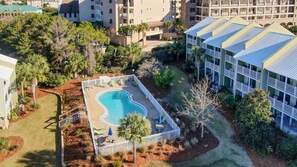 Vista aerea di un hotel con piscina, circondato da un recinto bianco, palme e un prato curato.