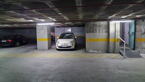 Un parking avec des piliers en béton, des lignes jaunes et une voiture blanche garée dans une place.