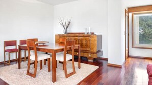 Un coin repas avec une table et des chaises en bois, un meuble avec des tiroirs et une fenêtre donnant sur les arbres.