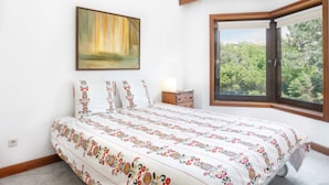 Une chambre à coucher avec un grand lit, une table de chevet, un tableau au mur et une fenêtre donnant sur des arbres.