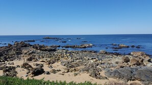 Une plage rocheuse avec une eau d’un bleu limpide et un navire visible au loin.