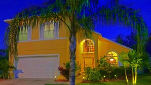 A two-story house with a garage, a large arched window, and a well-maintained lawn with palm trees. - Adventure Villa - Heated Pool & Spa - Themed Rooms - Min. to Disney - Game room (Davenport)