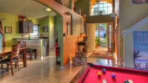 A spacious living area with a pool table, a dining area with wooden furniture, and a kitchen with a bar. - Adventure Villa - Heated Pool & Spa - Themed Rooms - Min. to Disney - Game room (Davenport)