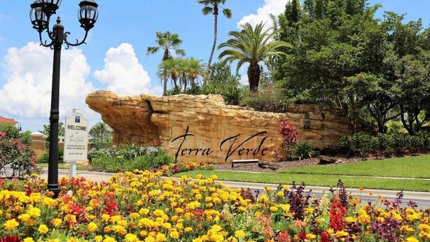 Un cartell de benvinguda per Terra Verde, amb una gran formació rocosa i flors de colors al primer pla.