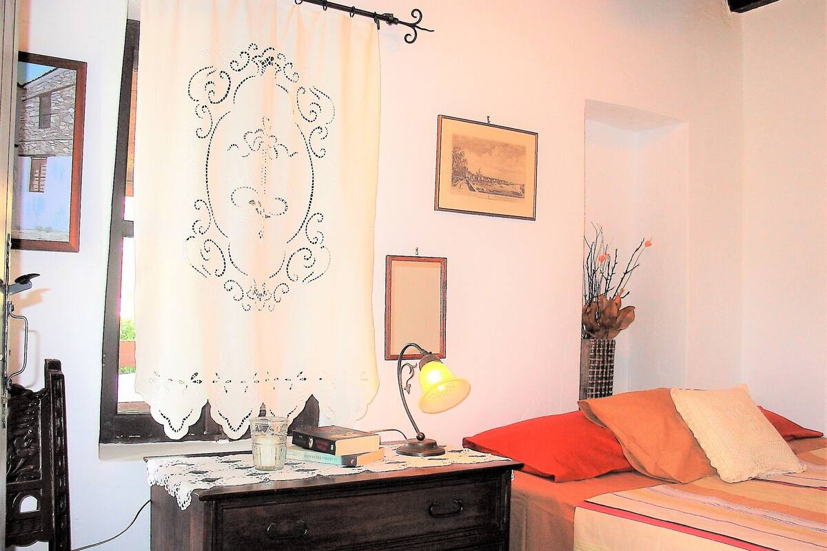 A bedroom with a bed, a nightstand, a lamp, a mirror, and a window with curtains.