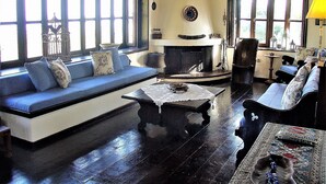 A traditional living room with a fireplace, wooden floors, and large windows. - Ampelos Estate (Aigialeia)