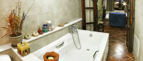 A bathroom with a large bathtub, a shower, a toilet, and a sink. There is a potted plant and various toiletries on the sink shelf.