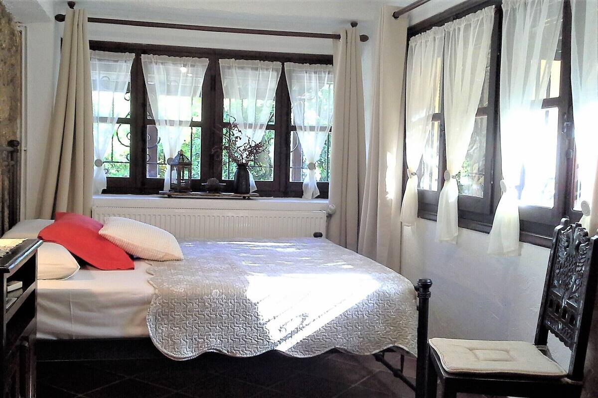 A bedroom with a bed, a nightstand, a lamp, and a window with curtains.