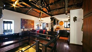 A spacious room with a wooden ceiling, a large painting on the wall, and a dining area with a table and chairs. - Ampelos Estate (Aigialeia)