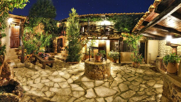A stone courtyard with a central fountain, surrounded by potted plants and rustic wooden furniture. - Ampelos Estate (Aigialeia)