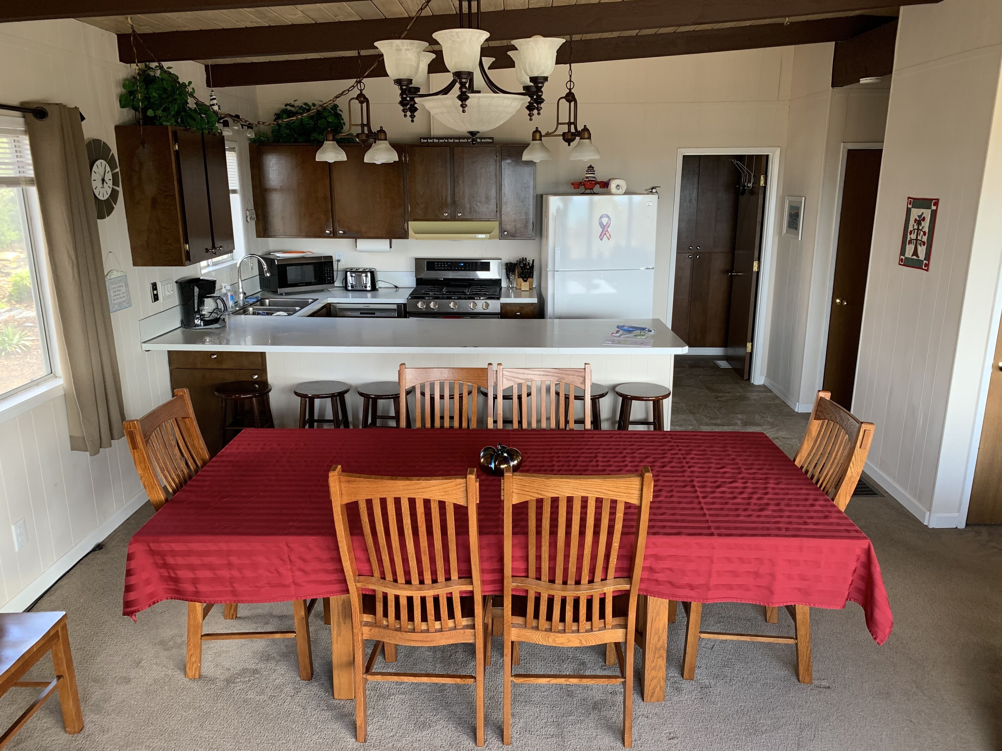 A kitchen with a central island, wooden chairs, and a red tablecloth.