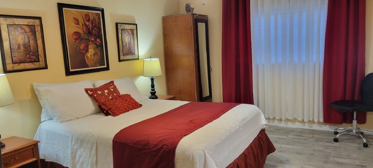 A hotel room with a bed, a nightstand, a lamp, a chair, and a wardrobe.