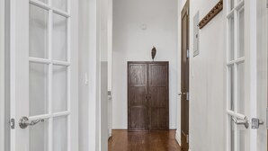 A hallway with white-framed doors, wooden flooring, and a dark wooden door at the end.