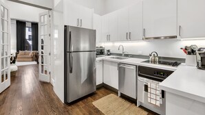 A modern kitchen with white cabinets, stainless steel appliances, and a wooden floor.