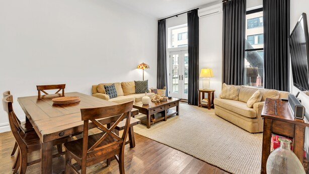 A modern living room with a wooden dining table, two sofas, and a TV.
