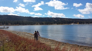 A lake with a dock and a forested hill in the background. - Expansive Lake View Home1 mile from the Village w/ Hot tub & Game Rm VRR20250487 (Big Bear Lake)