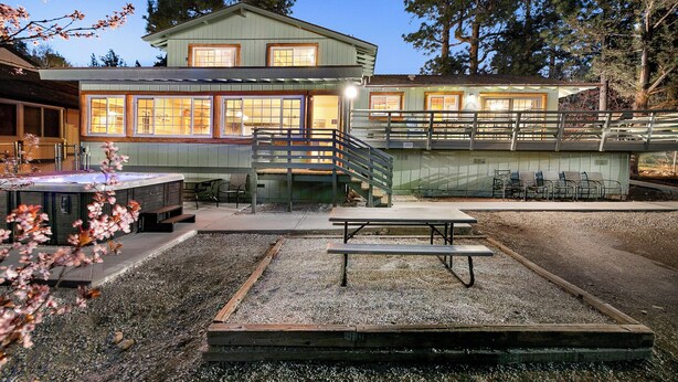 A two-story building with a covered patio area, outdoor seating, and a hot tub. - Expansive Lake View Home1 mile from the Village w/ Hot tub & Game Rm VRR20250487 (Big Bear Lake)
