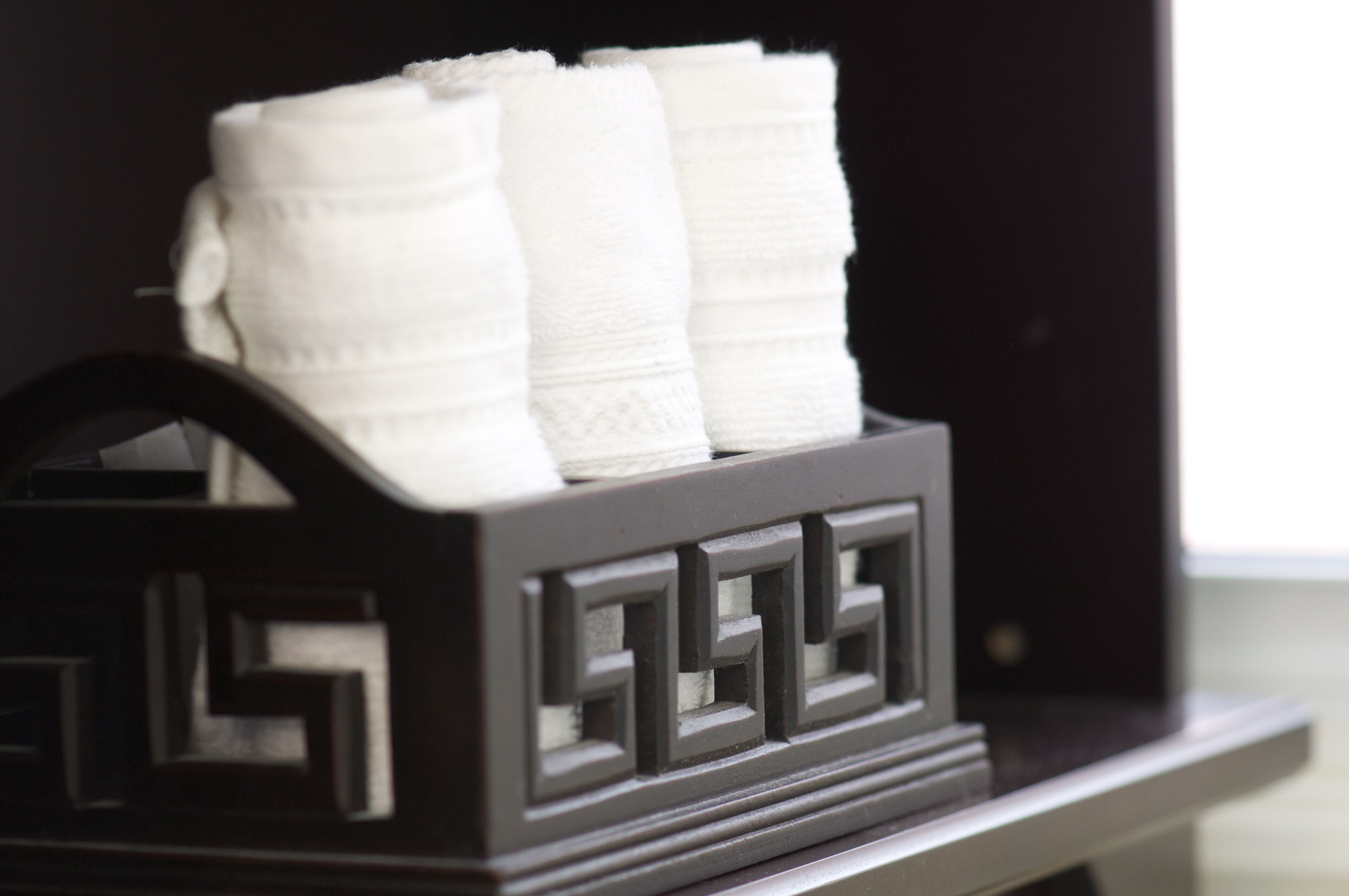 A black storage box with a geometric design, containing neatly folded white towels.