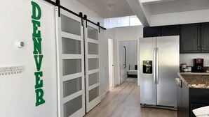 A modern kitchen with a sliding door labeled "DENVER," a stainless steel refrigerator, and a coffee maker on the counter.