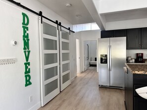 A modern kitchen with a sliding door labeled "DENVER," a stainless steel refrigerator, and a coffee maker on the counter. - Penthouse in heart of Capitol Hill , Uptown (Denver)