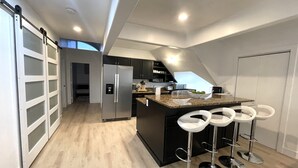 A modern kitchen with a central island, bar stools, and a sliding door.