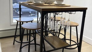 A dining area with a table set for four, a view of the cityscape through a large window, and a modern design with black metal legs and wooden surfaces.
