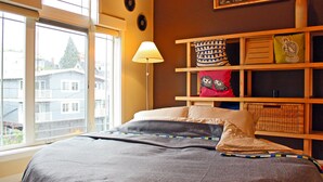 Un dormitorio con cama, lámpara de noche, ventana y repisas con adornos.