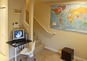 A home office with a computer desk, a chair, a map on the wall, and a staircase.