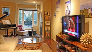 Una sala de estar con un piano de cola, un televisor, una mesa de centro de vidrio y una estantería.