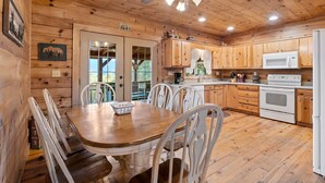 A wooden cabin interior with a dining table, chairs, kitchen area, and a ceiling fan.