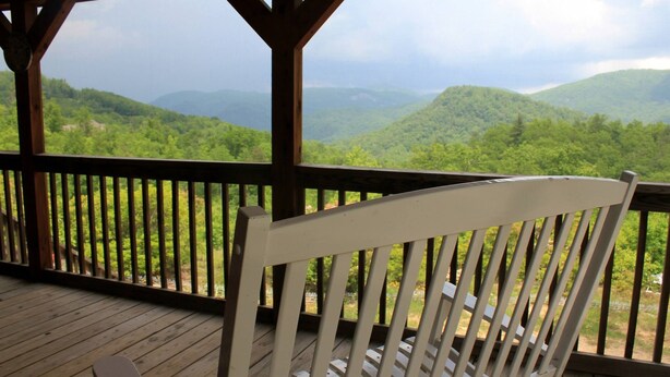 A wooden deck with a white chair, overlooking a mountainous landscape.
