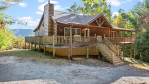 A log cabin with a porch, a staircase, and a view of the mountains.