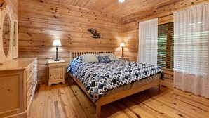 A wooden-paneled bedroom with a bed, nightstands, and a ceiling fan.