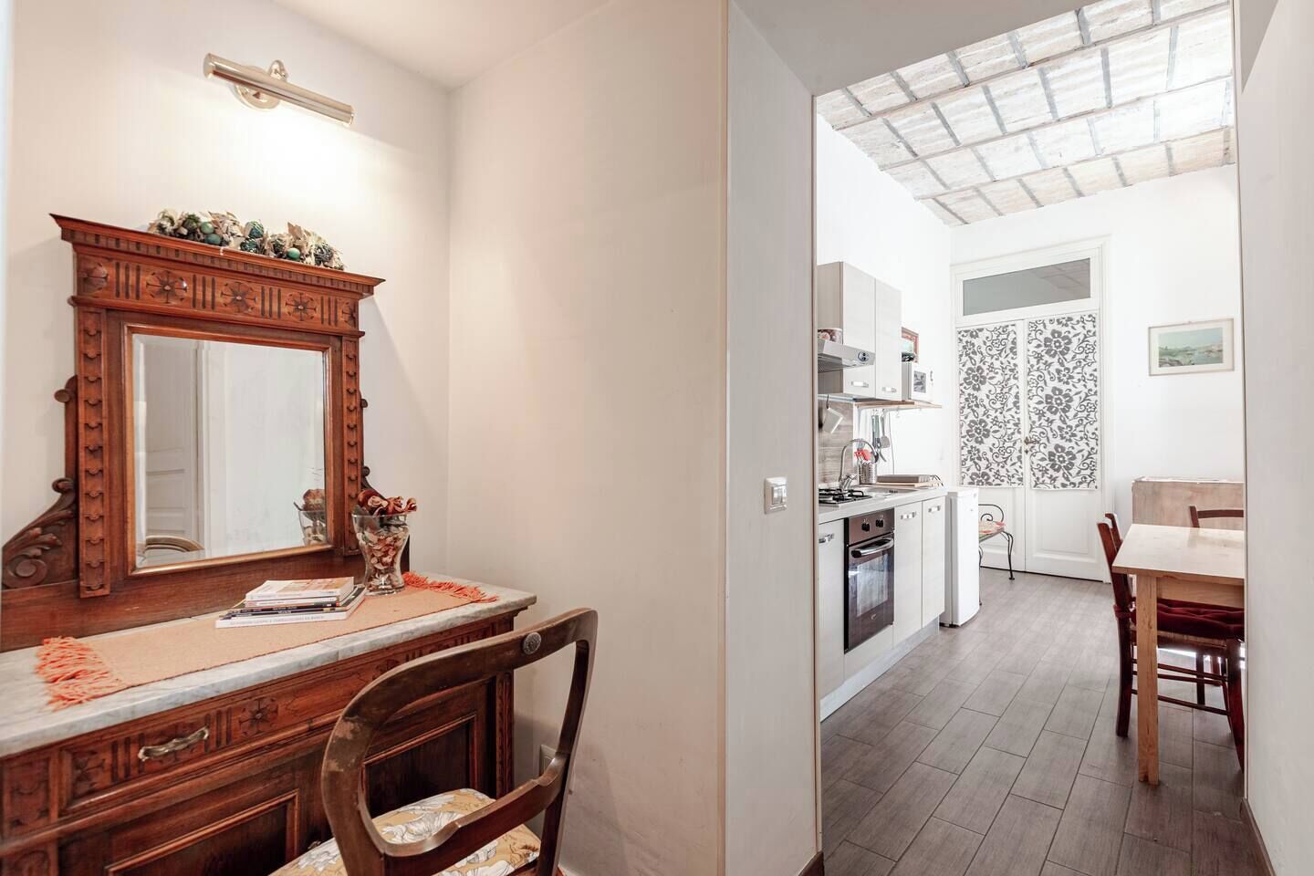 A compact kitchen with white cabinets, a small dining area with a wooden table and chairs, and a large mirror above the counter.