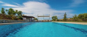 A swimming pool with lounge chairs and a covered area, surrounded by palm trees and a stone wall. - Villa Mathea  - Spacious Villa With Privacy And Private Large Swimming Pool (Chania)