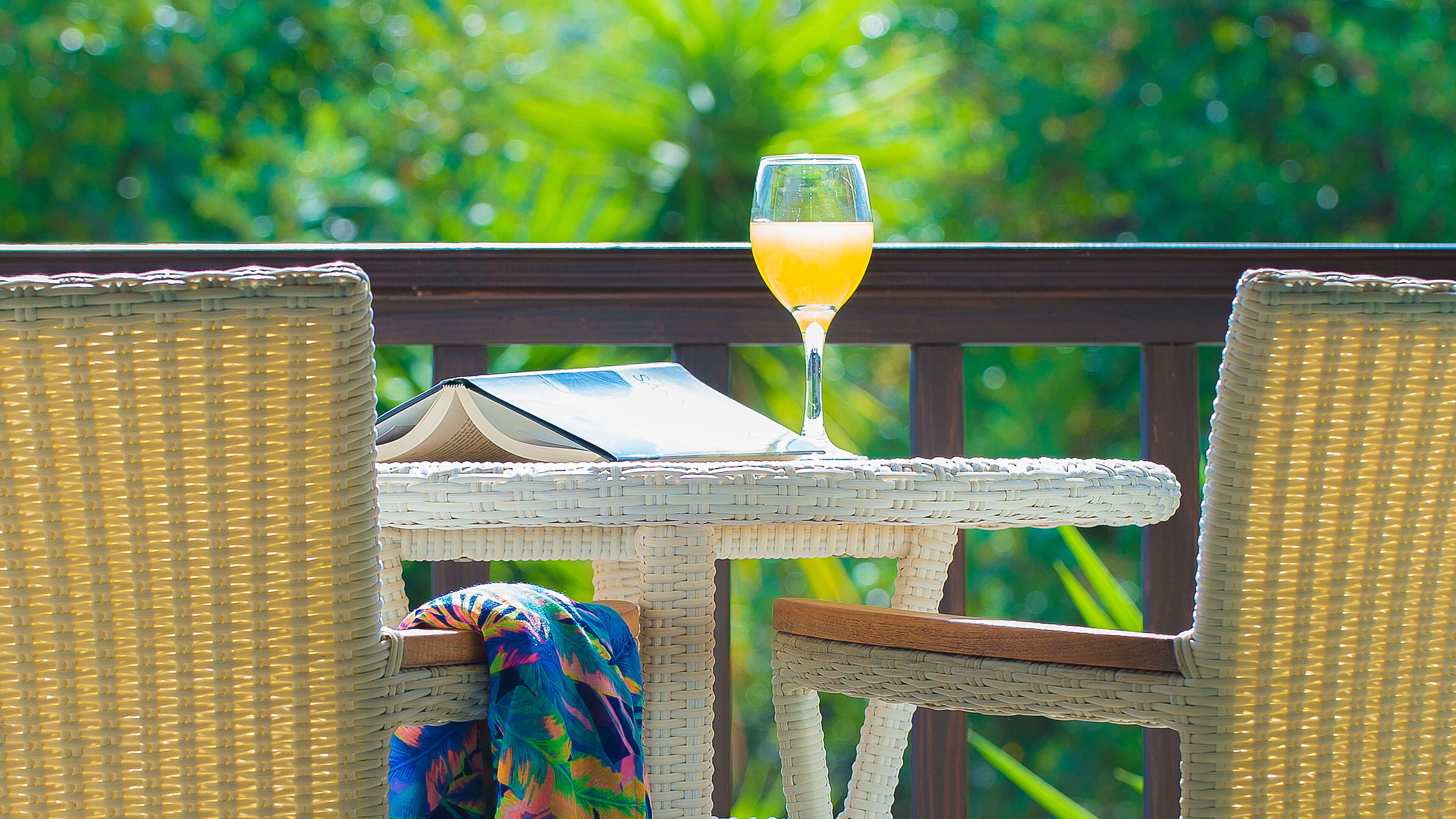 A wicker table with a glass of orange juice, a book, and a colorful cloth.