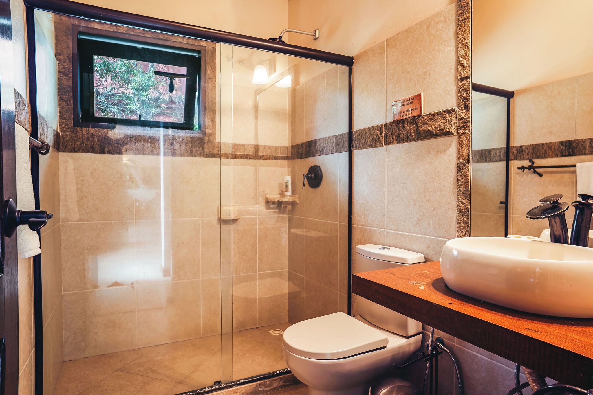 Un baño con cabina de ducha de vidrio, inodoro blanco, lavamanos con encimera de madera y un espejo.