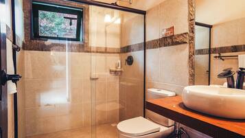 Un baño con cabina de ducha de vidrio, inodoro blanco, lavamanos con encimera de madera y un espejo.