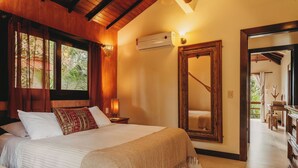 A bedroom with a large bed, a nightstand, a wall-mounted air conditioner, and a mirror.
