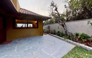 A house with a tiled roof, a stone patio, and a garden with various plants and a tree.