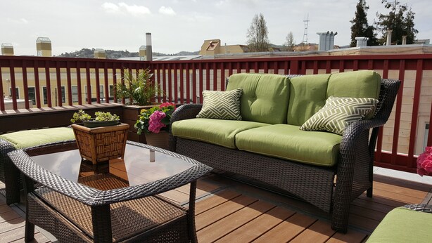 Eine Dachterrasse mit Korbmöbeln, einem Glastisch und Blumentöpfen.