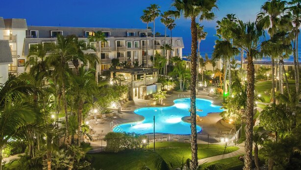 A hotel with a pool area, palm trees, and a view of the ocean at dusk. - North Coast A101 Corner condo West & South Facing Ocean views from Two Balconies (Oceanside)