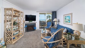 A living room with a television, wicker furniture, a sofa, a fireplace, and a view of the outdoors. - North Coast A101 Corner condo West & South Facing Ocean views from Two Balconies (Oceanside)