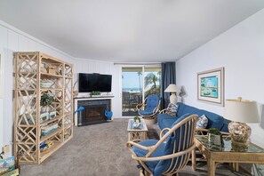 A living room with a television, wicker furniture, a sofa, a fireplace, and a view of the outdoors.