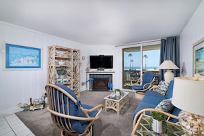 Een woonkamer met rieten meubels, een flatscreen televisie, een open haard en uitzicht op de oceaan.