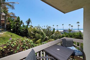 A balcony with a view of the beach, palm trees, and a building in the background. - North Coast A101 Corner condo West & South Facing Ocean views from Two Balconies (Oceanside)