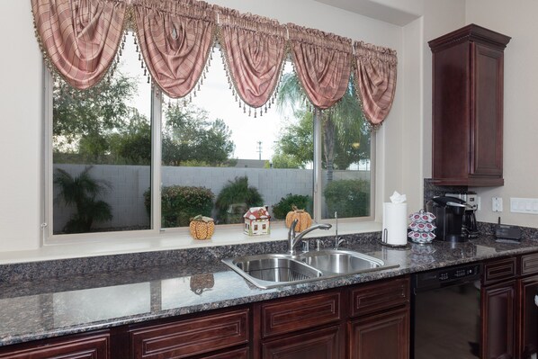 A kitchen with a granite countertop, stainless steel sink, and wooden cabinets.