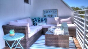 Un espace extérieur accueillant, aménagé avec des meubles en osier, une petite table ronde et un panneau décoratif portant l’inscription « HOME » sur le mur.